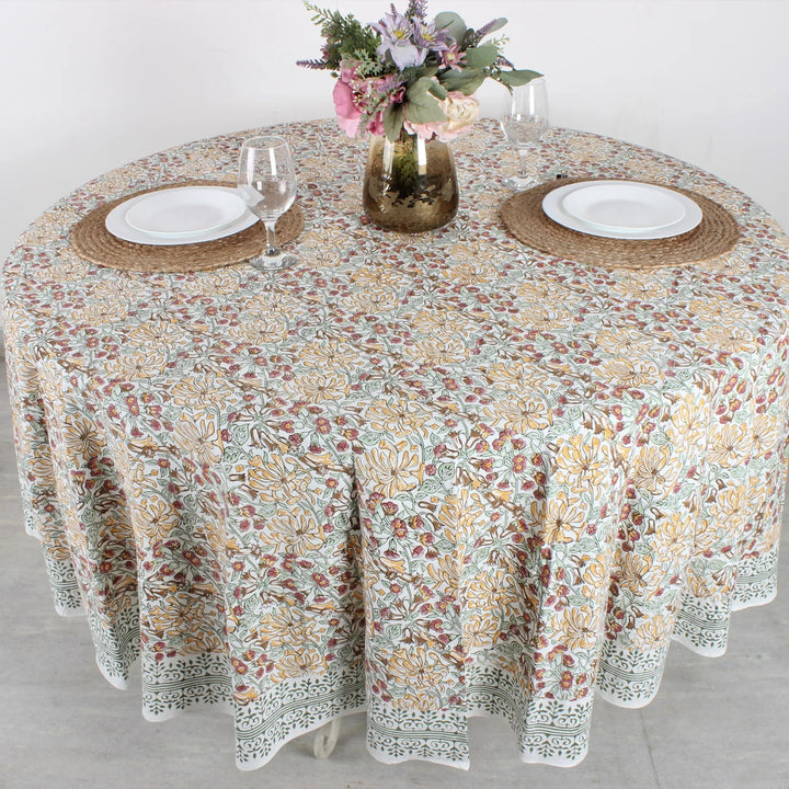 Round table with floral patterned tablecloth, plates, and glasses on a light background