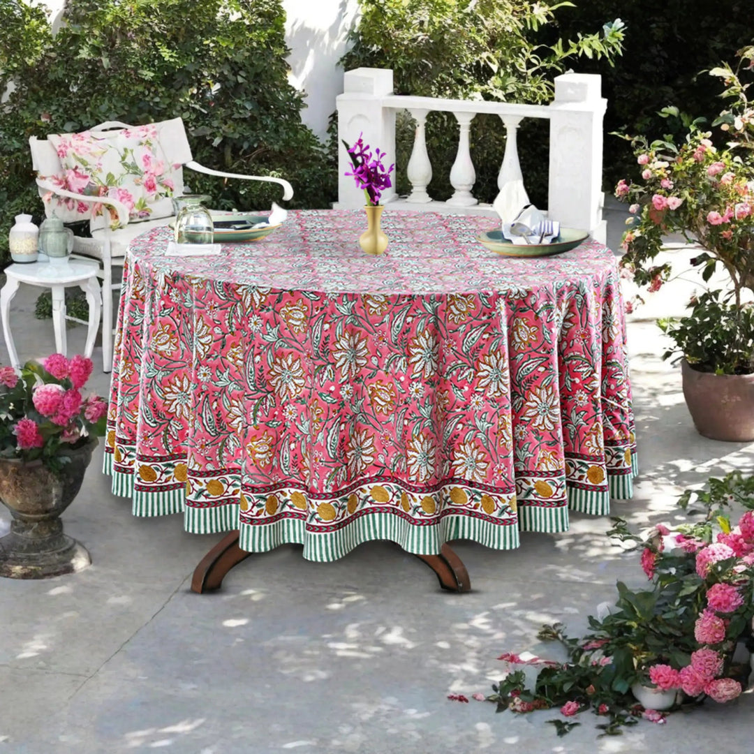 Outdoor setting with a floral tablecloth on a round table, surrounded by plants and chairs.