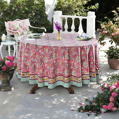 Outdoor setting with a floral tablecloth on a round table, surrounded by plants and chairs.