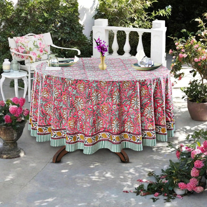 Outdoor setting with a floral tablecloth on a round table, surrounded by plants and chairs.