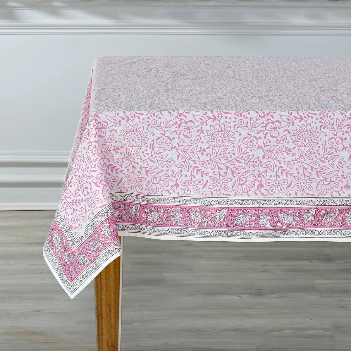 Tablecloth with pink and white floral pattern on a wooden table against a gray wall.