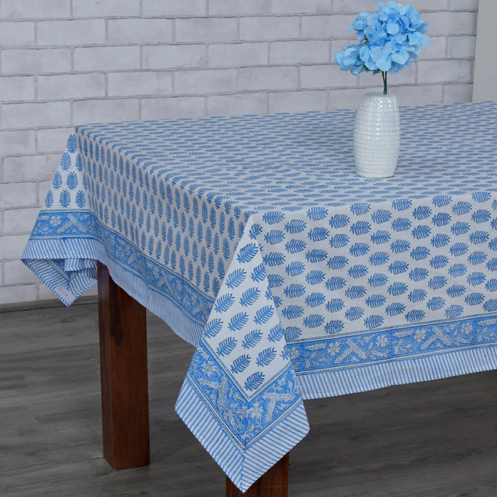 Blue and white patterned tablecloth on a wooden table with a vase of flowers against a brick wall.