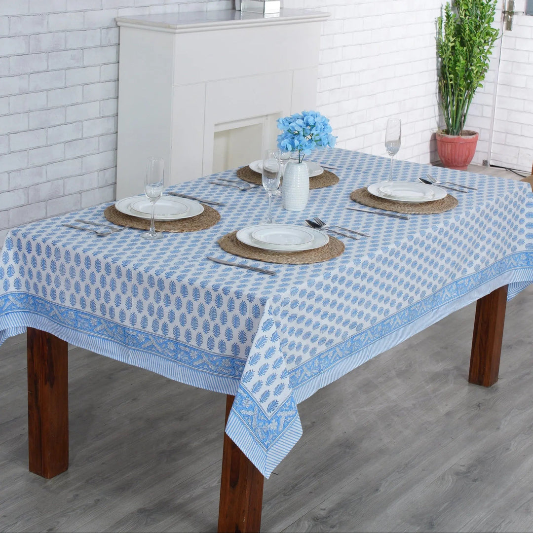 Dining table with a blue and white checkered tablecloth in a room with a fireplace and plants.