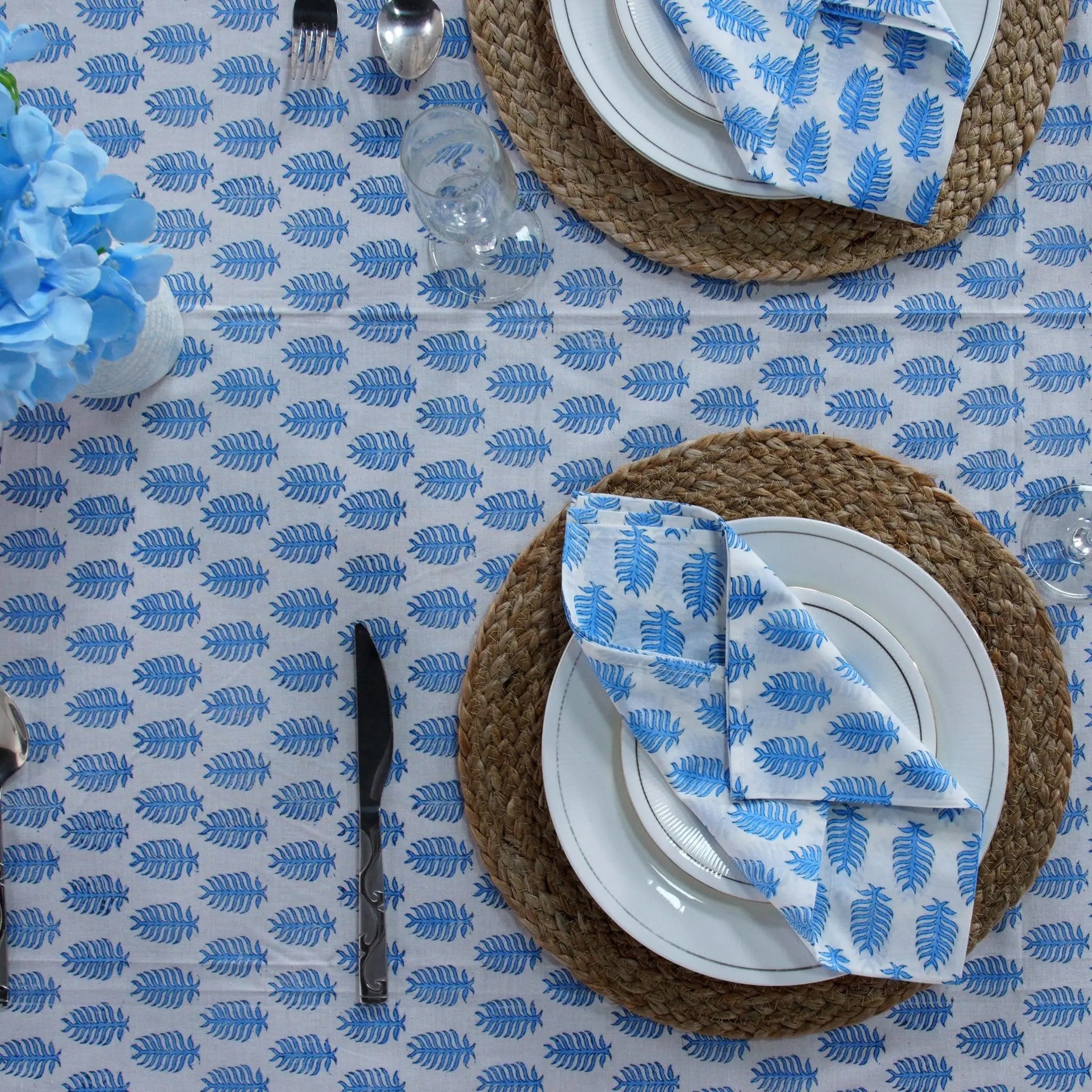 Table setting with blue and white patterned tablecloth, plates, and cutlery.