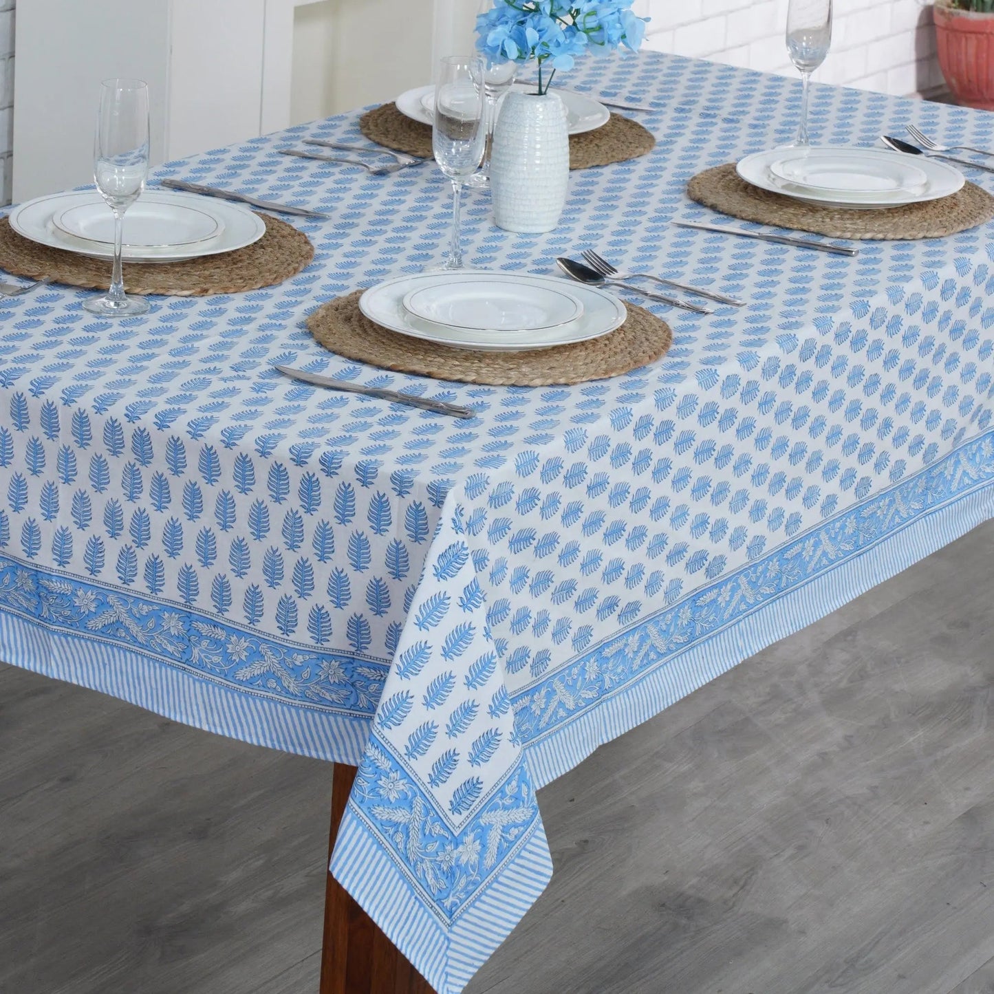 Dining table set with a blue and white patterned tablecloth, plates, and cutlery.