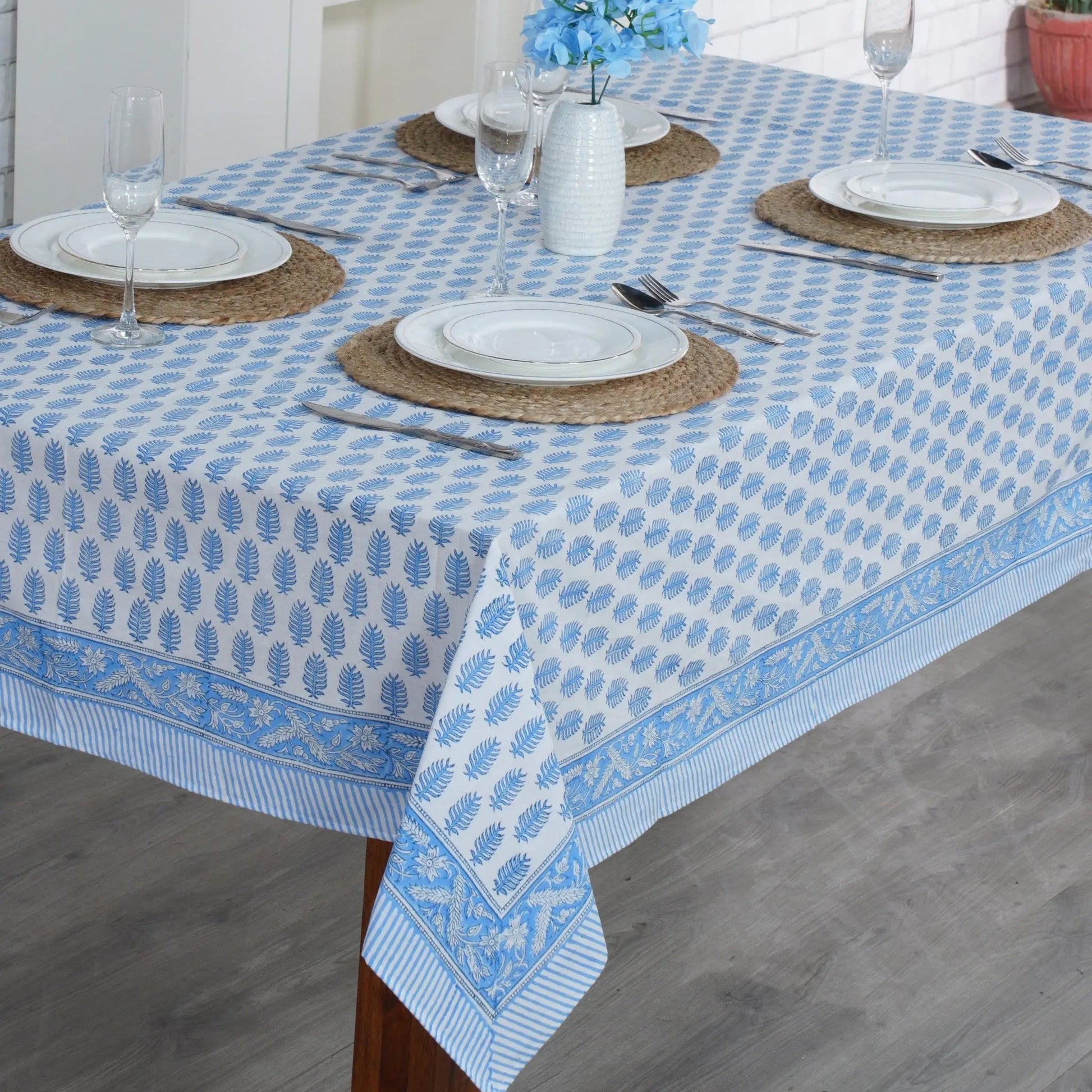 Dining table set with a blue and white patterned tablecloth, plates, and cutlery.