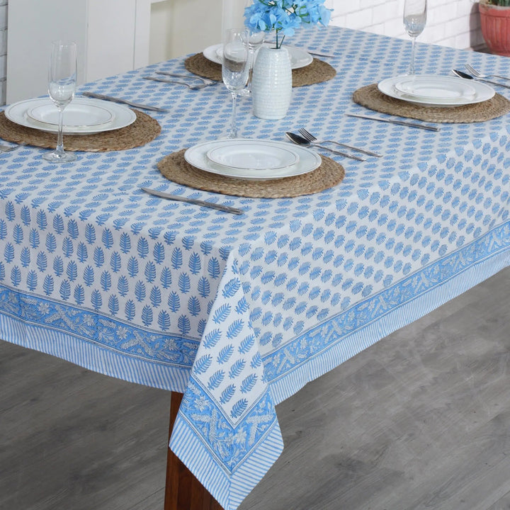 Dining table set with a blue and white patterned tablecloth, plates, and cutlery.
