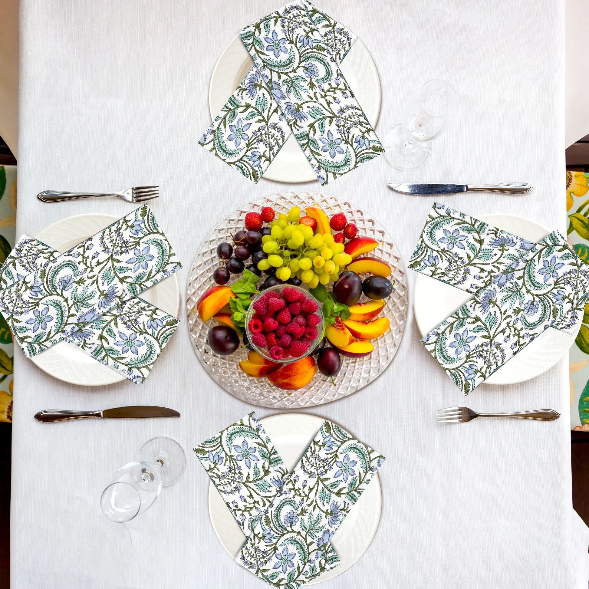 Table setting with patterned plates, napkins, and a fruit platter on a white tablecloth.