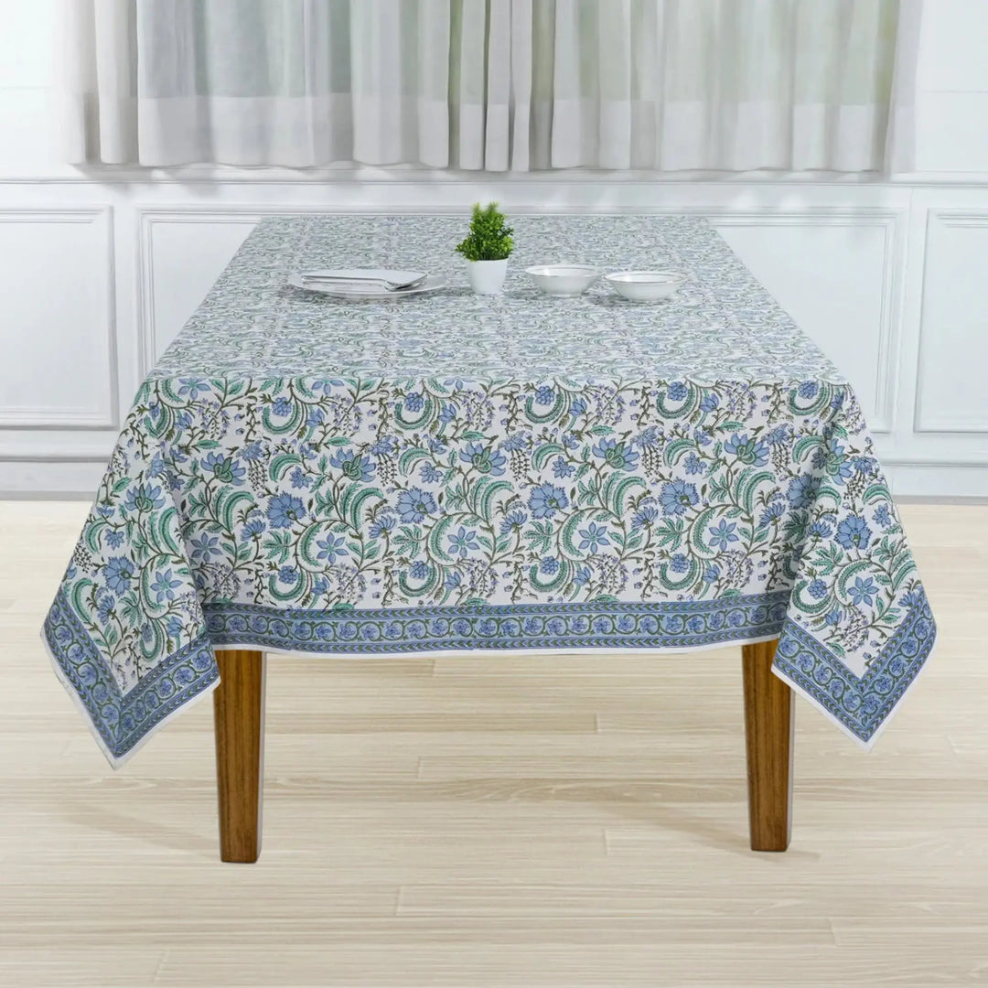 Tablecloth with floral pattern on a wooden table in a room with white walls and curtains.