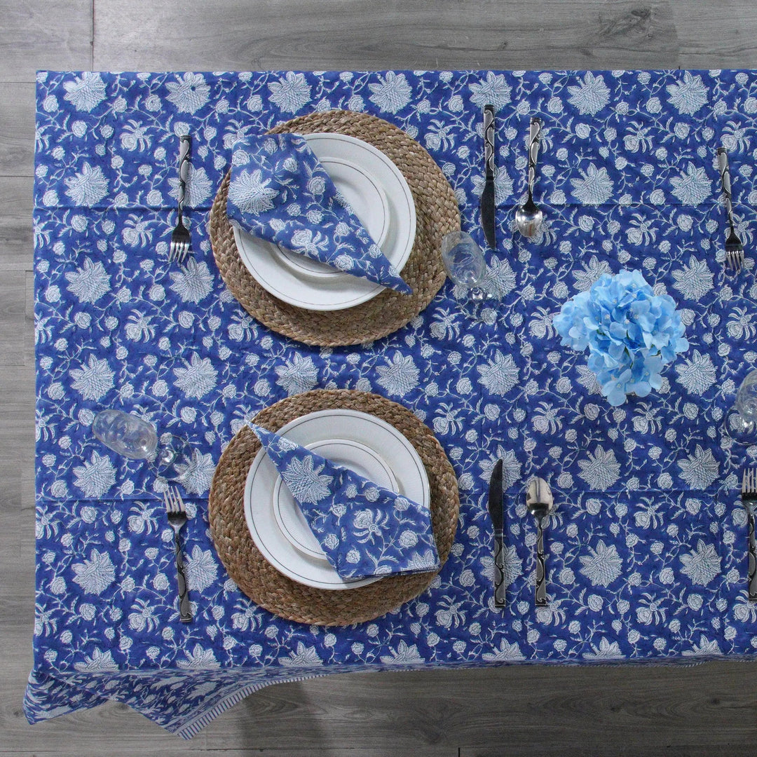 Table setting with blue floral placemat, white plates, and silverware on a wooden table.
