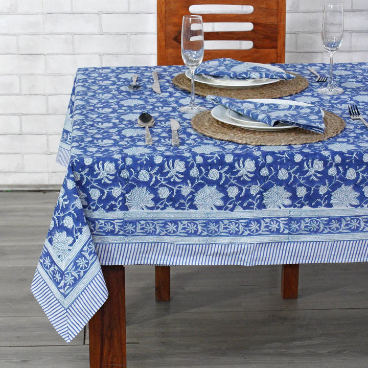 Dining table set with a blue floral patterned tablecloth on a wooden table.