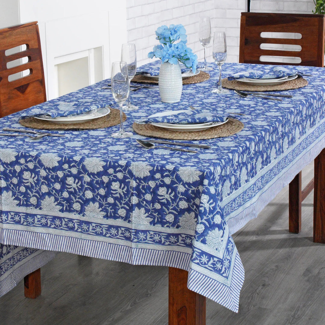 Dining table set with a blue floral tablecloth, glasses, and plates.