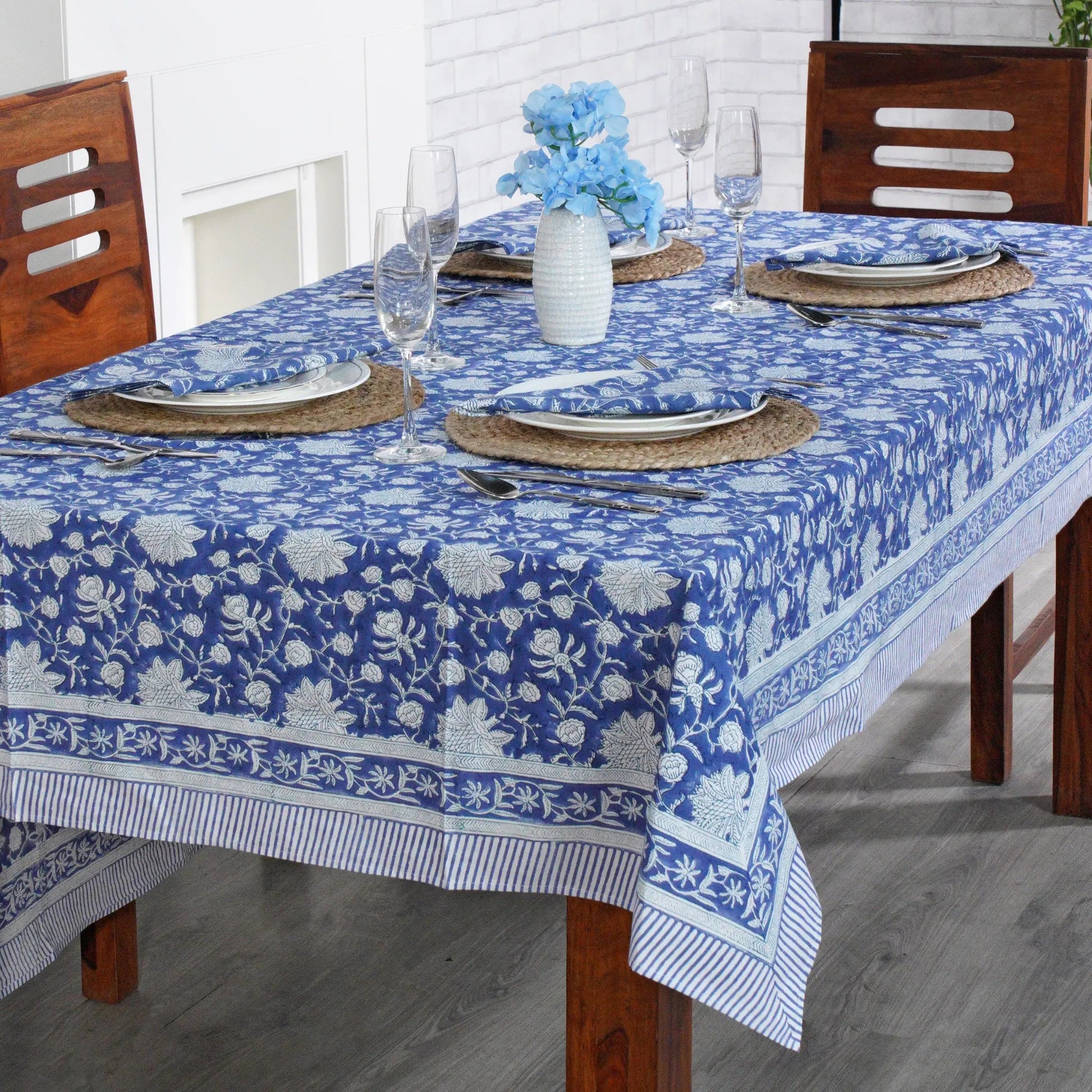 Dining table set with a blue floral tablecloth, glasses, and plates.