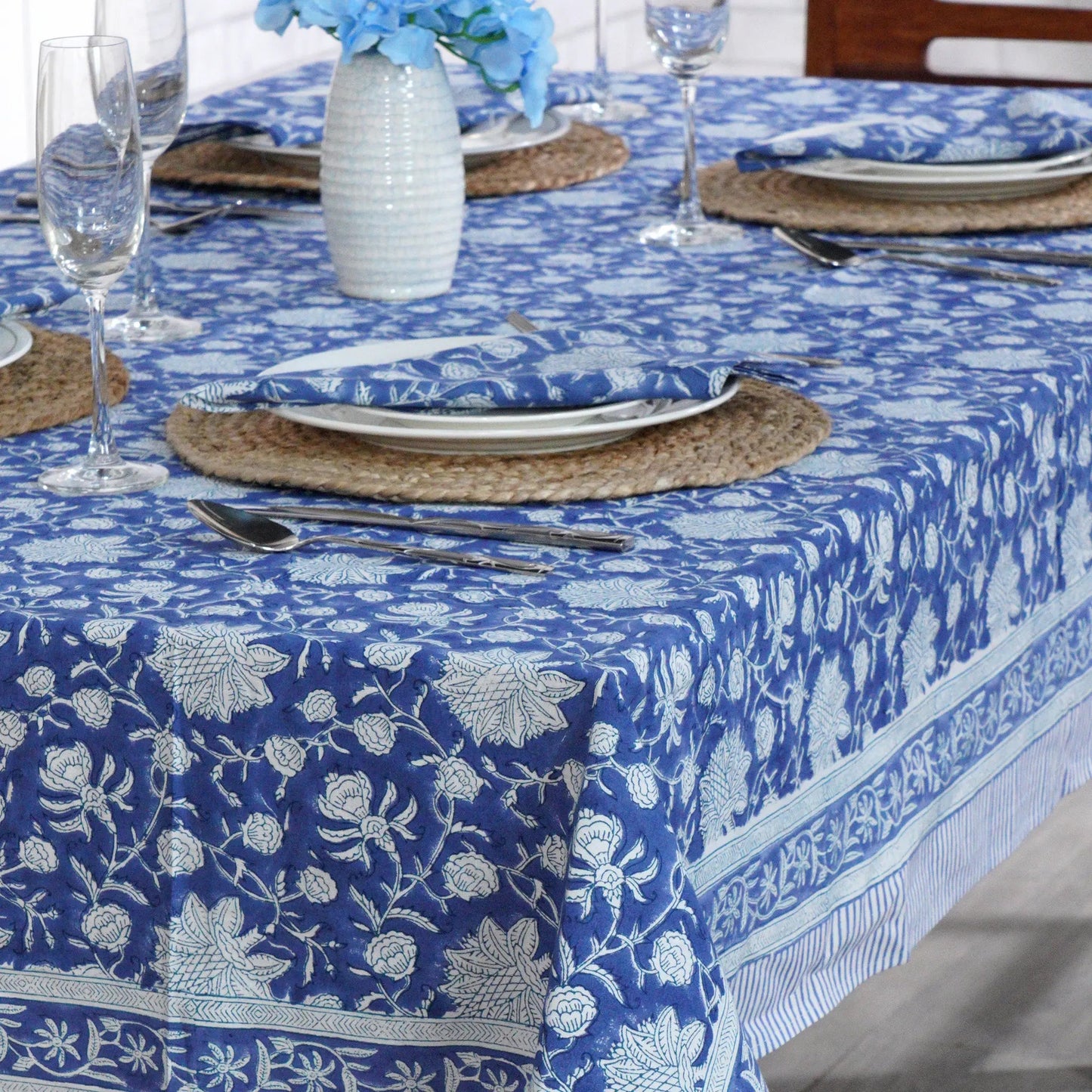 Dining table set with blue floral tablecloth, plates, and cutlery.