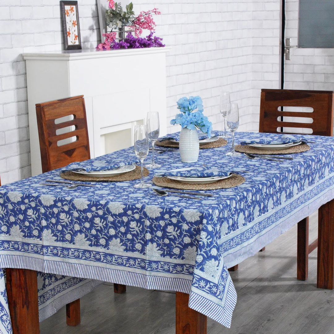 Dining table set with a blue floral tablecloth in a room with white brick walls.