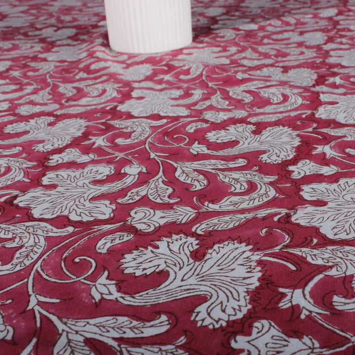 Red fabric with white floral patterns, partially covering a white cylindrical object.