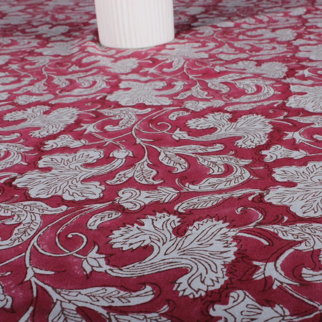 Red fabric with white floral patterns, partially covering a white cylindrical object.