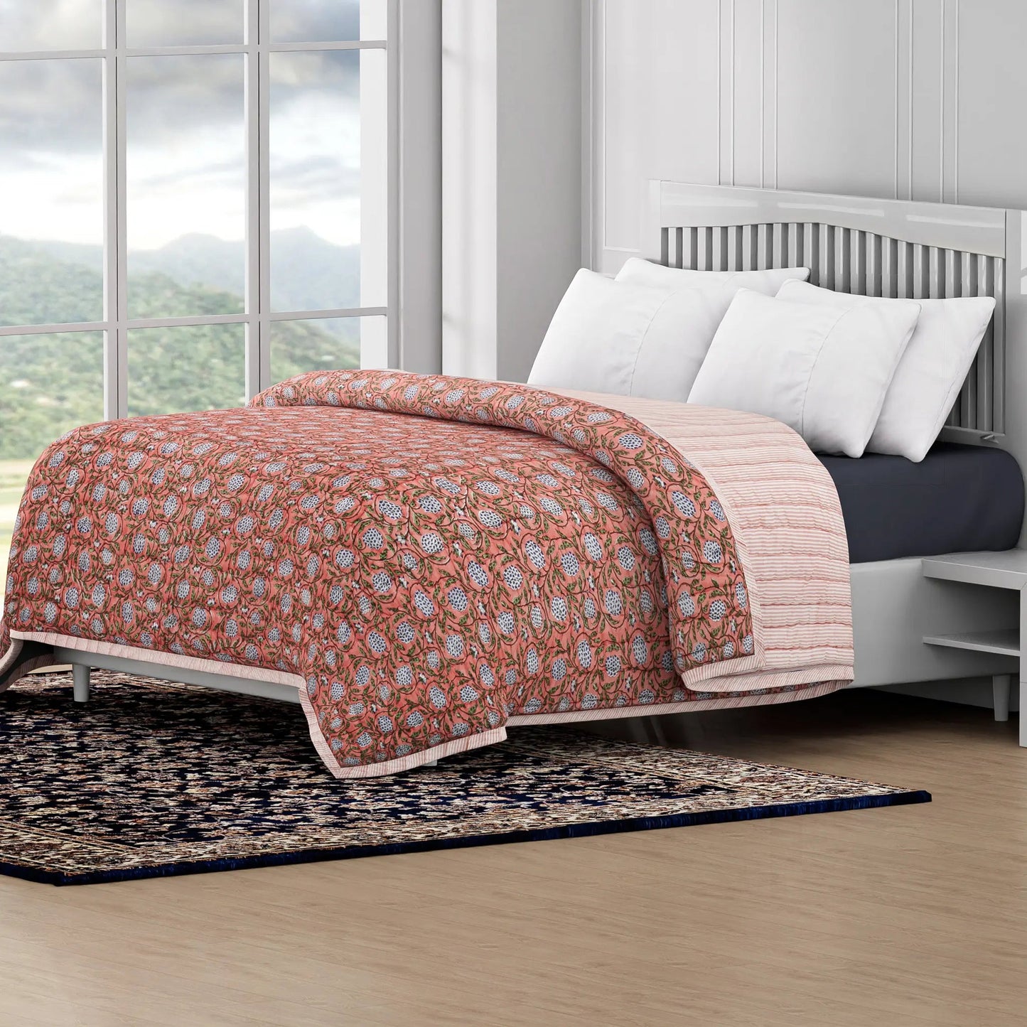 Bed with floral quilt and white pillows in a room with large windows and a view of mountains.