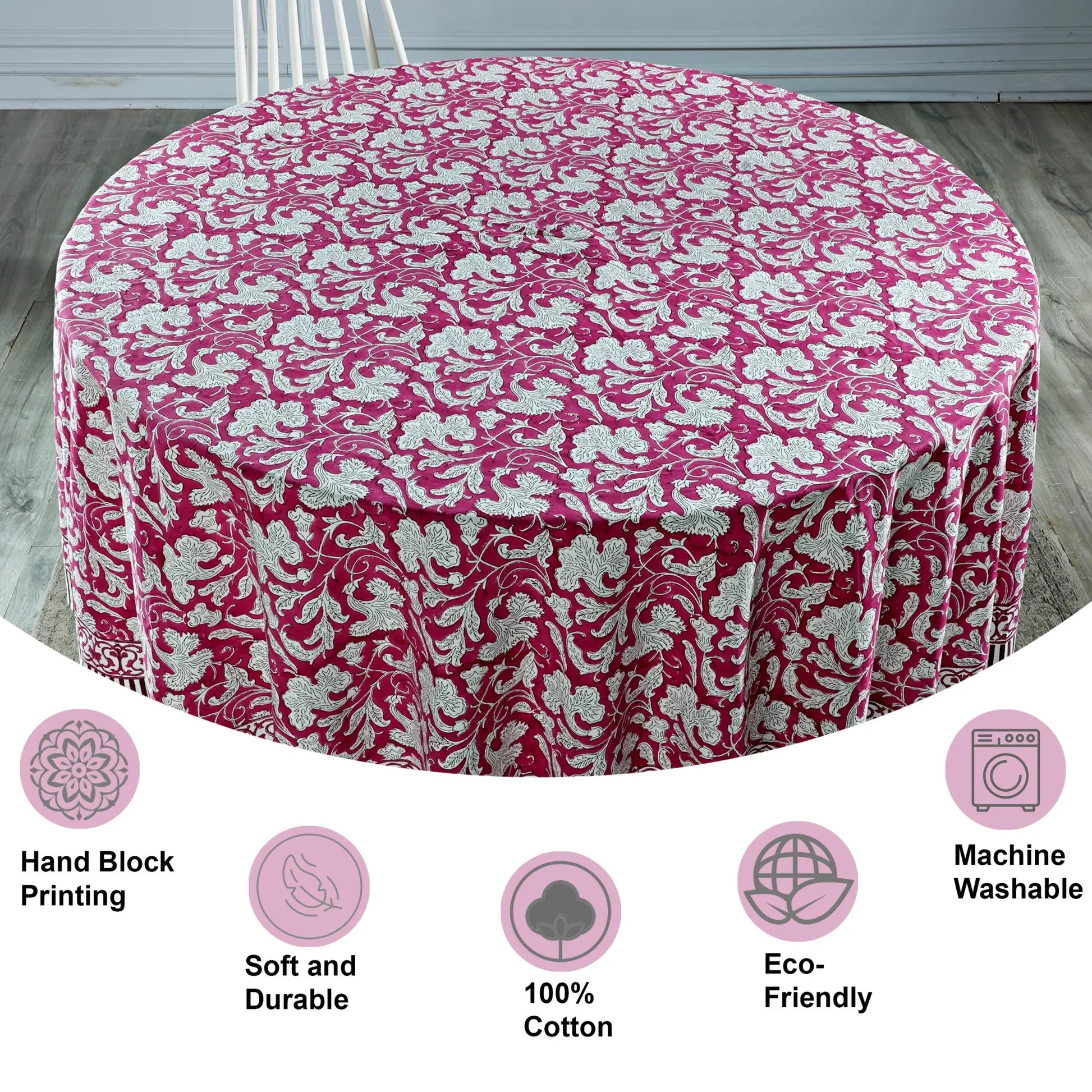 Round table covered with a pink floral tablecloth on a wooden floor.