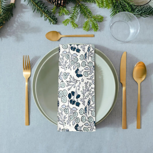 Table setting with a floral-patterned napkin, gold cutlery, and greenery on a gray tablecloth.