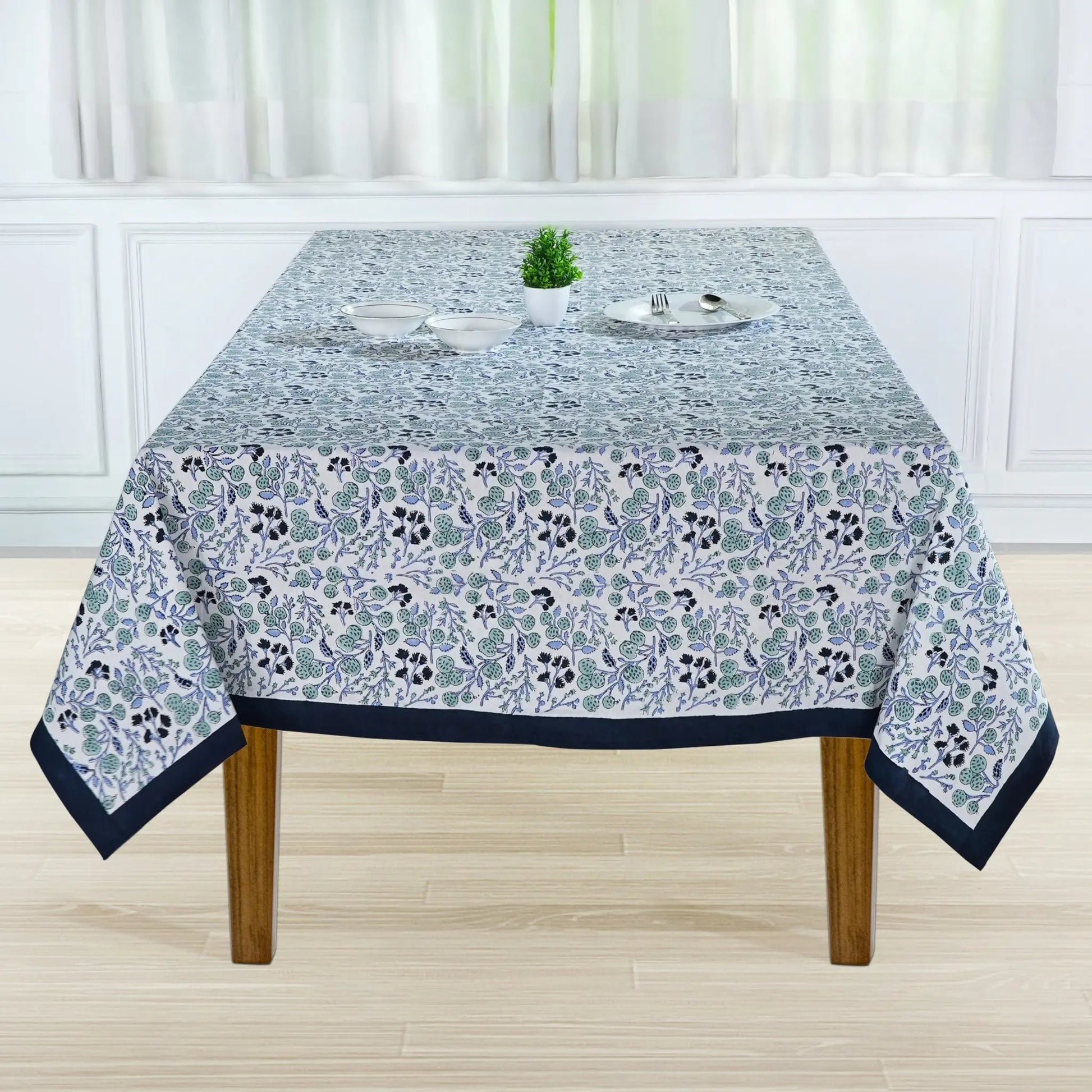 Tablecloth with floral pattern on a wooden table in a room with white walls and curtains.