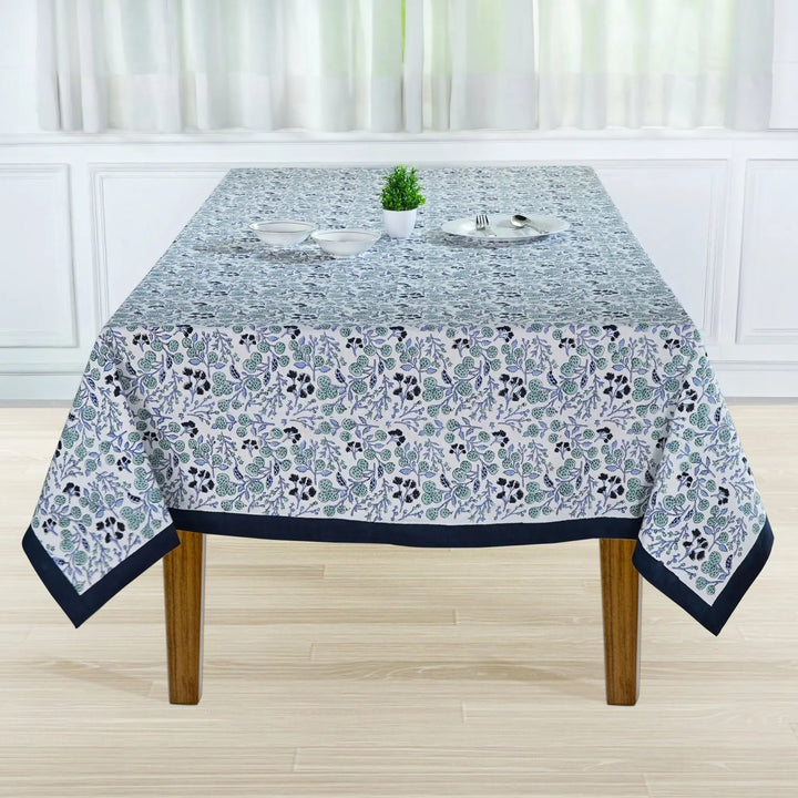 Tablecloth with floral pattern on a wooden table in a room with white walls and curtains.