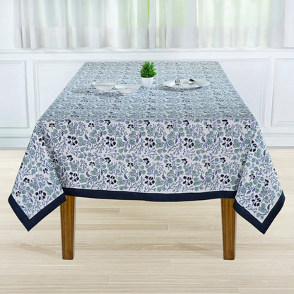 Tablecloth with floral pattern on a wooden table in a room with white walls and curtains.