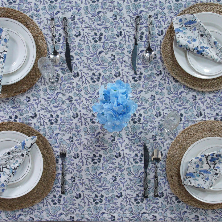 Table setting with floral tablecloth, plates, cutlery, and napkins on a patterned surface.