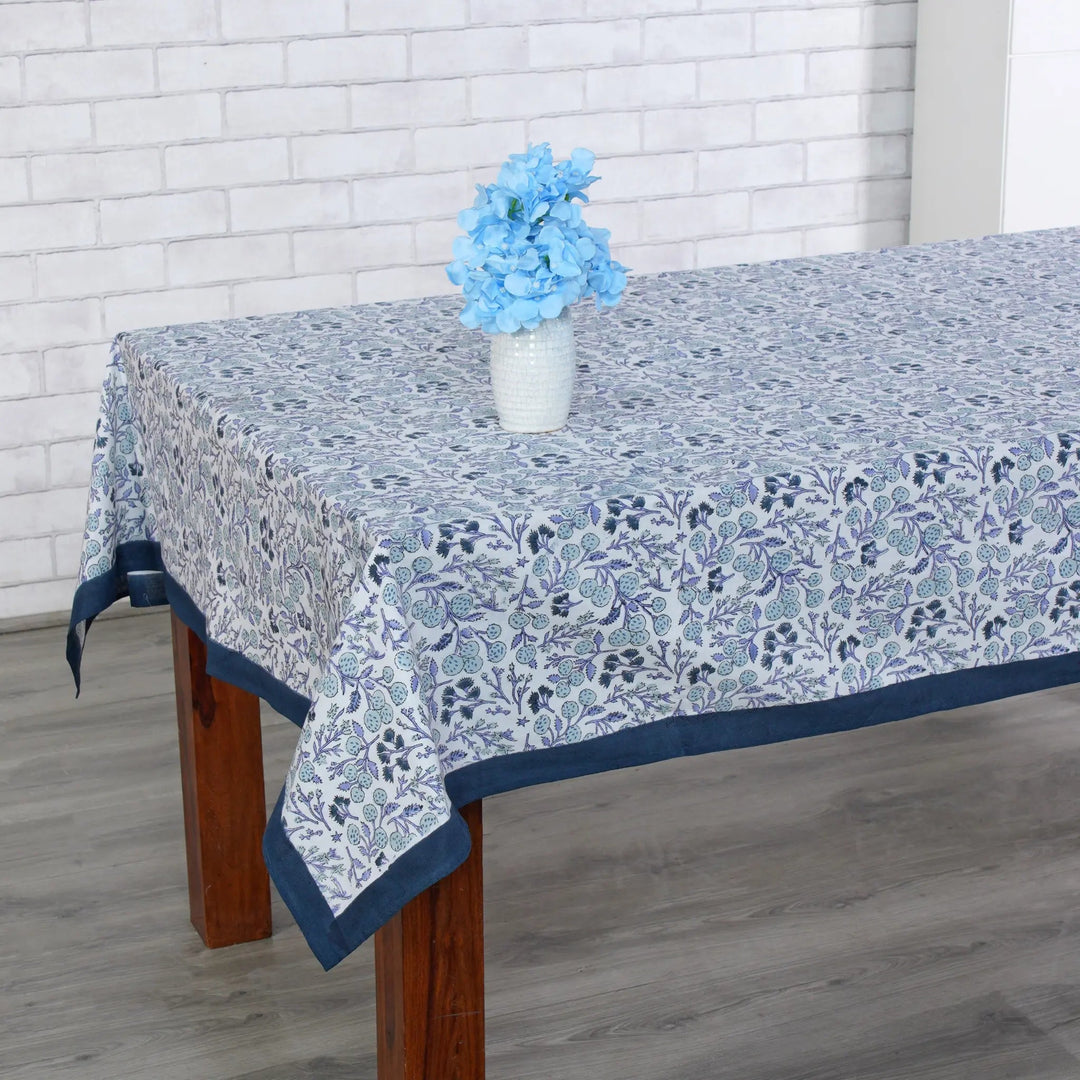 Tablecloth with floral pattern on a wooden table against a white brick wall.