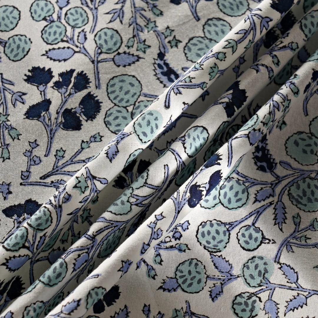 Close-up of floral patterned fabric with blue and green colors on a beige background.