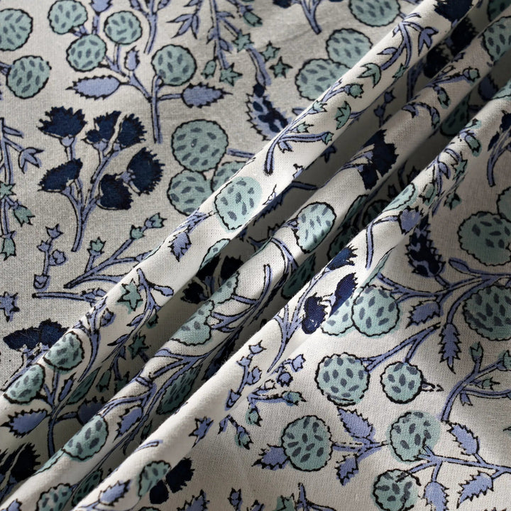 Close-up of floral patterned fabric with blue and green colors on a beige background.
