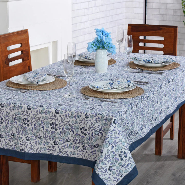 Dining table set with floral tablecloth, plates, glasses, and flowers.