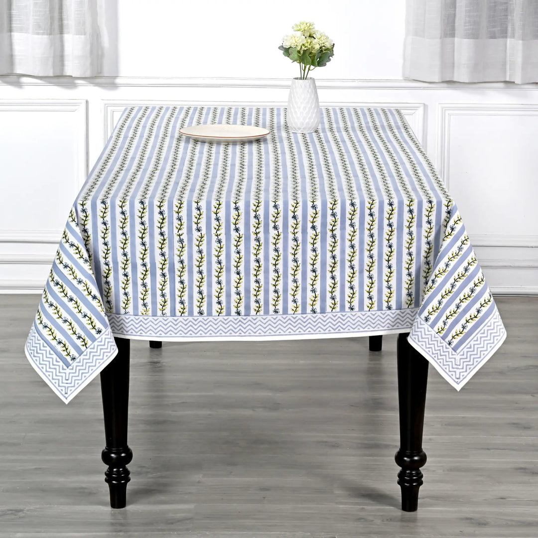 Tablecloth with floral pattern on a wooden table in a room with white curtains.