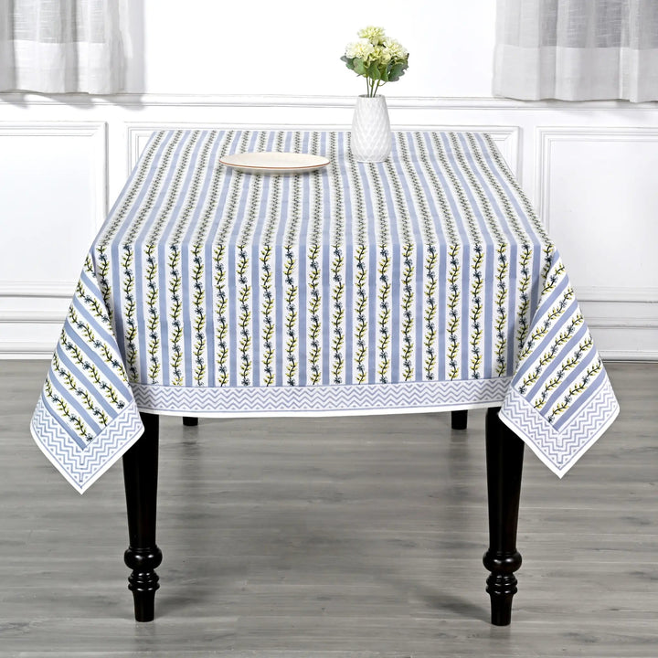 Tablecloth with floral pattern on a wooden table in a room with white curtains.