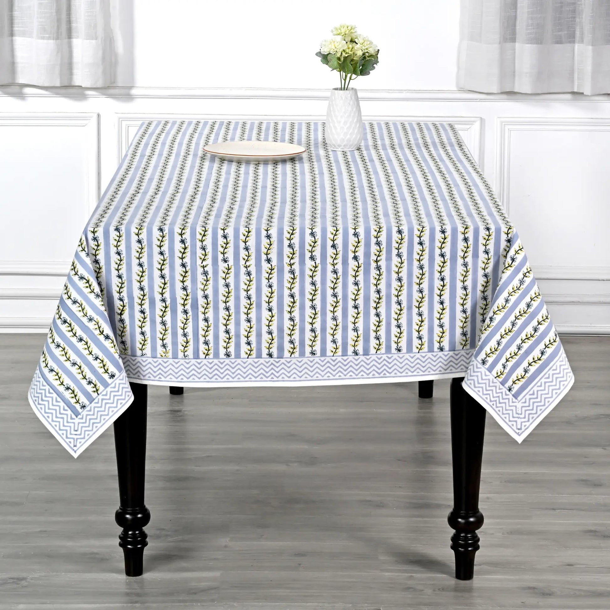 Tablecloth with floral pattern on a wooden table in a room with white curtains.