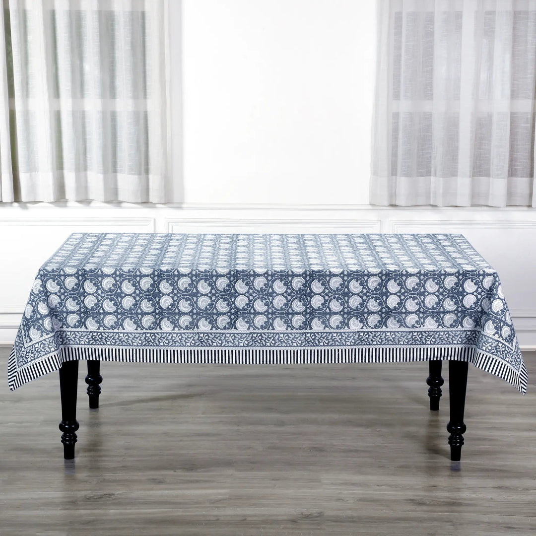 Tablecloth with blue and white pattern on a wooden table in a room with white curtains.