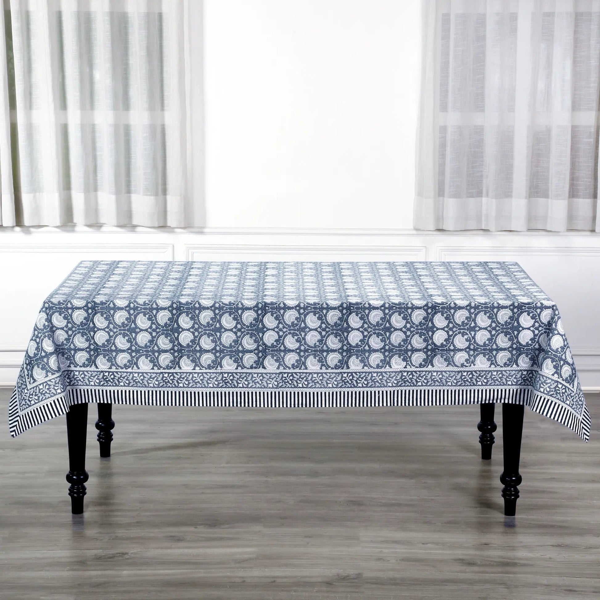 Tablecloth with blue and white pattern on a wooden table in a room with white curtains.
