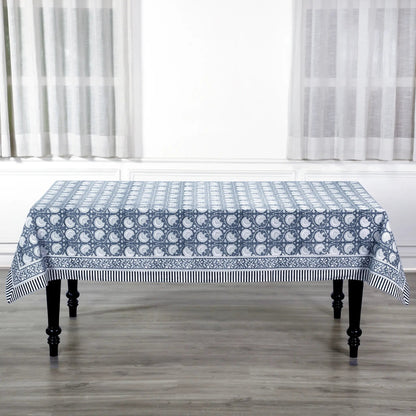 Tablecloth with blue and white pattern on a wooden table in a room with white curtains.