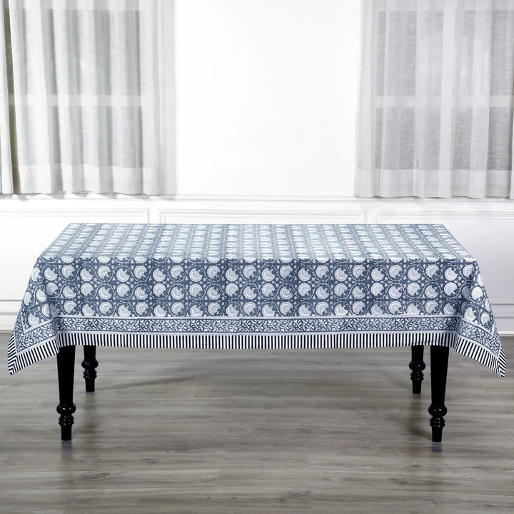 Tablecloth with blue and white pattern on a wooden table in a room with white curtains.