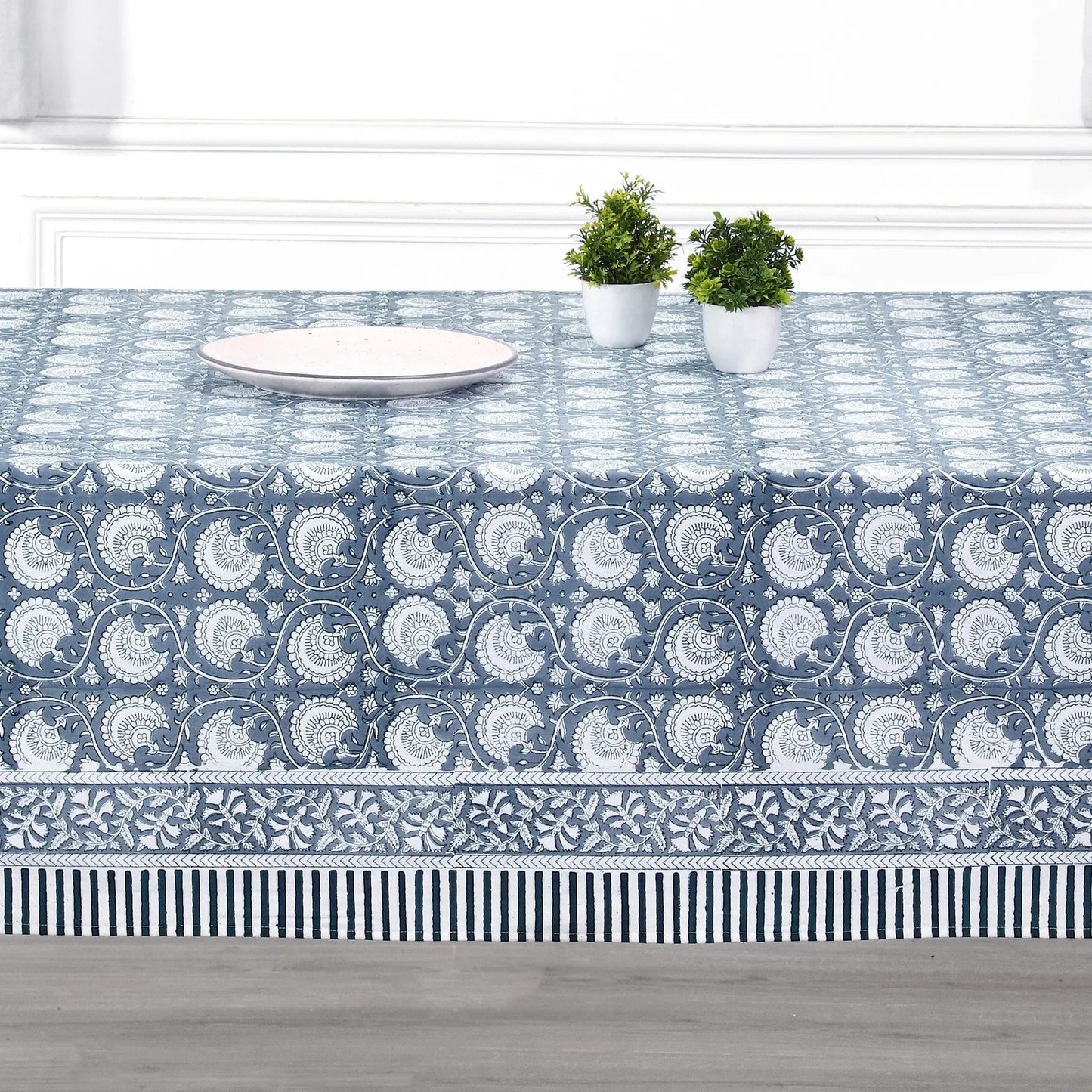Tablecloth with blue and white pattern on a table with plates and plants.