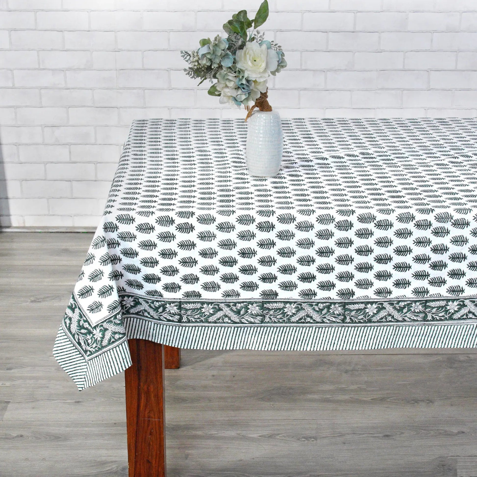 Tablecloth with leaf pattern on a wooden table against a white brick wall.