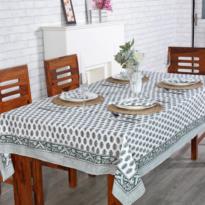 Dining table set with a patterned tablecloth, plates, and chairs in a room.