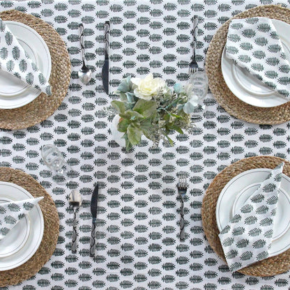Table setting with a leaf patterned tablecloth, white plates, and woven placemats.