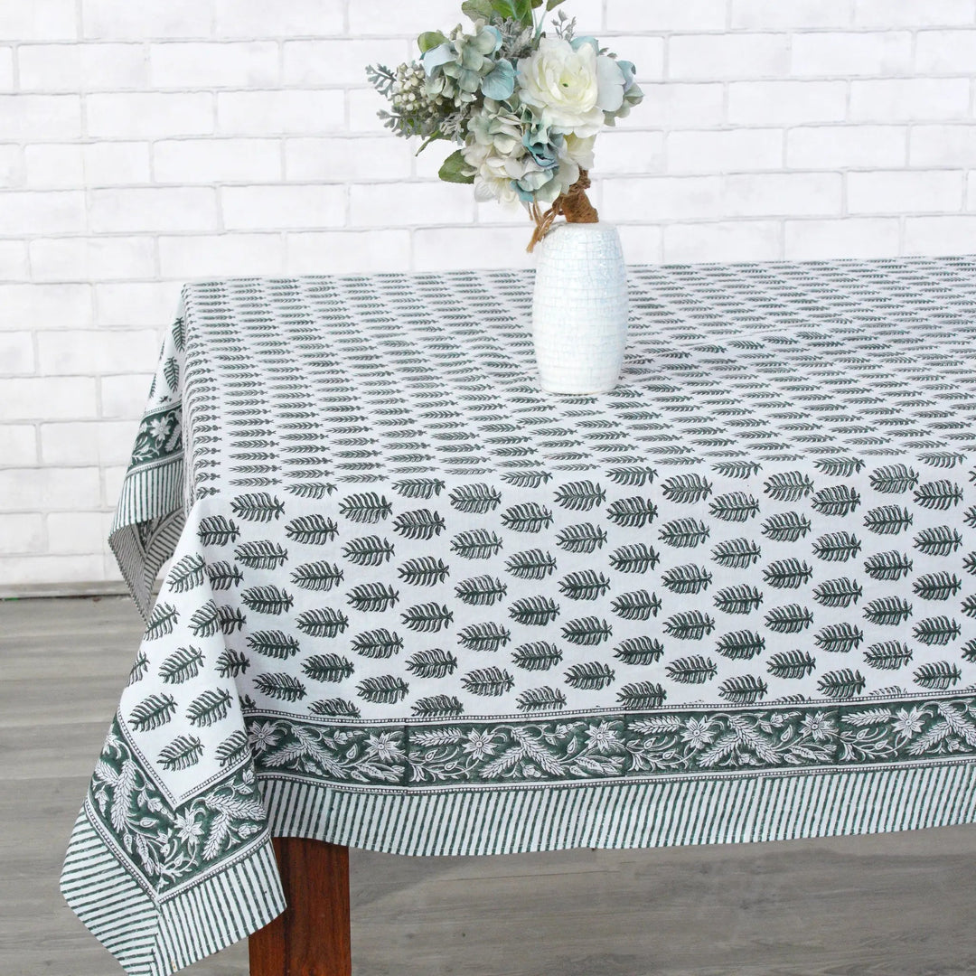 Tablecloth with leaf pattern on a wooden table against a white brick wall.