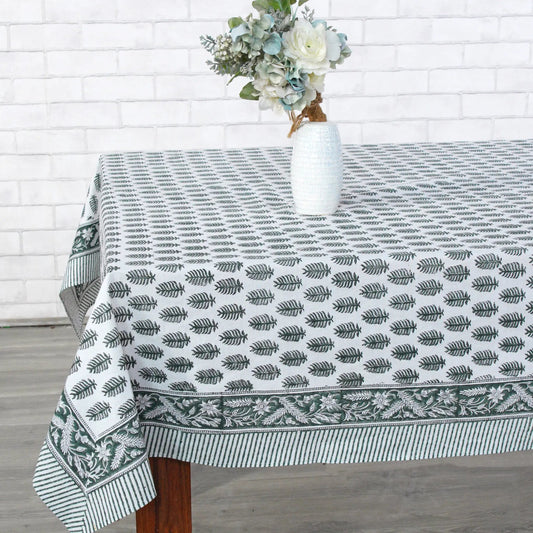 Tablecloth with leaf pattern on a wooden table against a white brick wall.