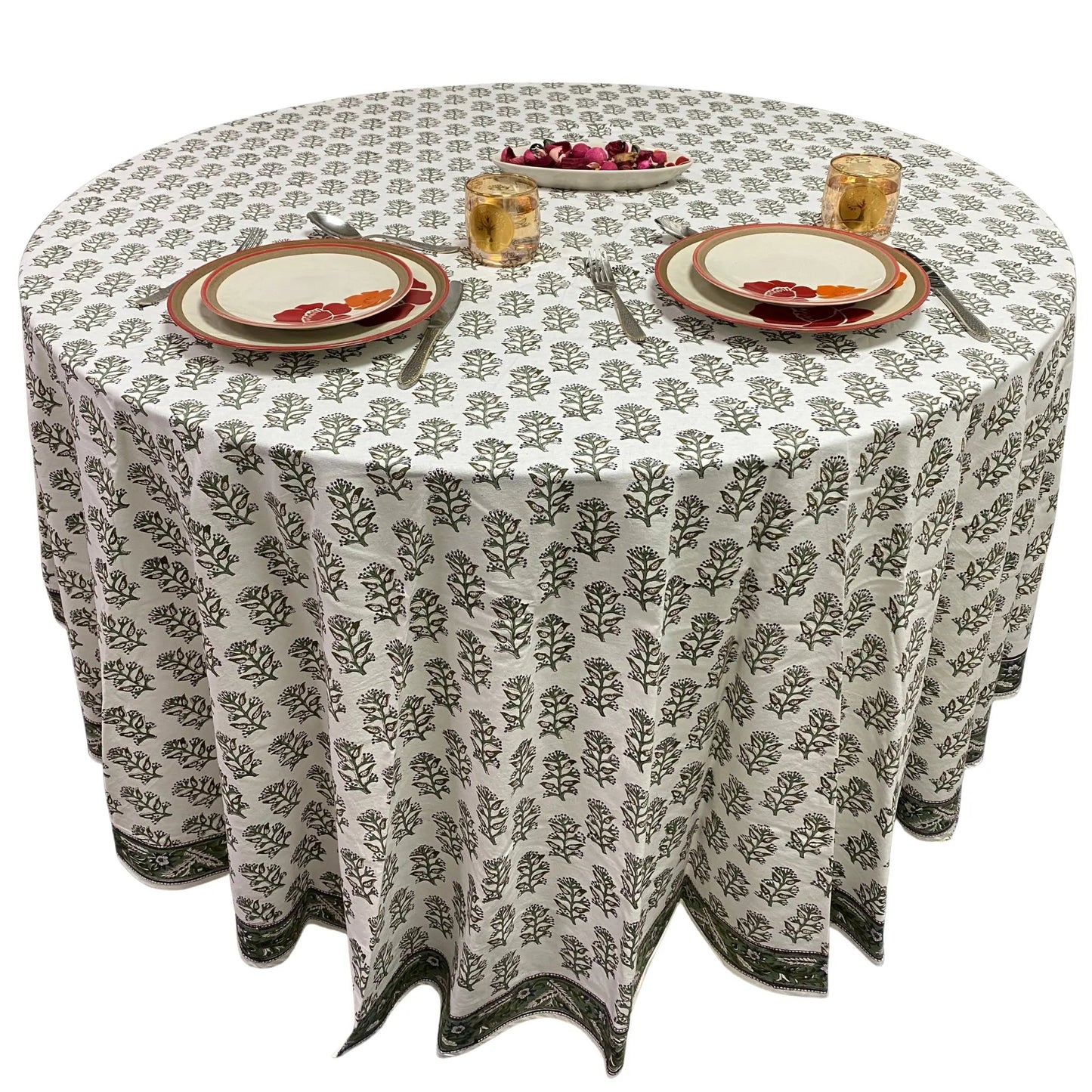 Round table with a patterned tablecloth, plates, and glasses on a white background
