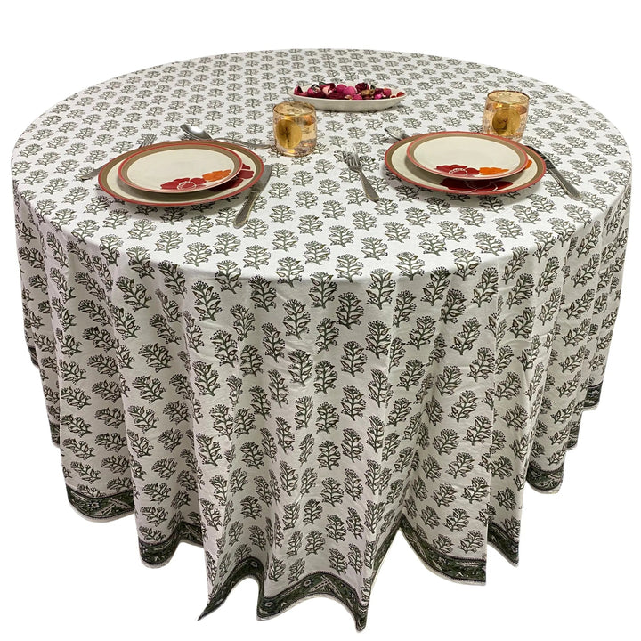 Round table with a patterned tablecloth, plates, and glasses on a white background