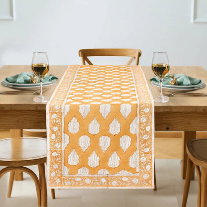 Dining table set with a yellow and white patterned table runner, glasses, and plates.