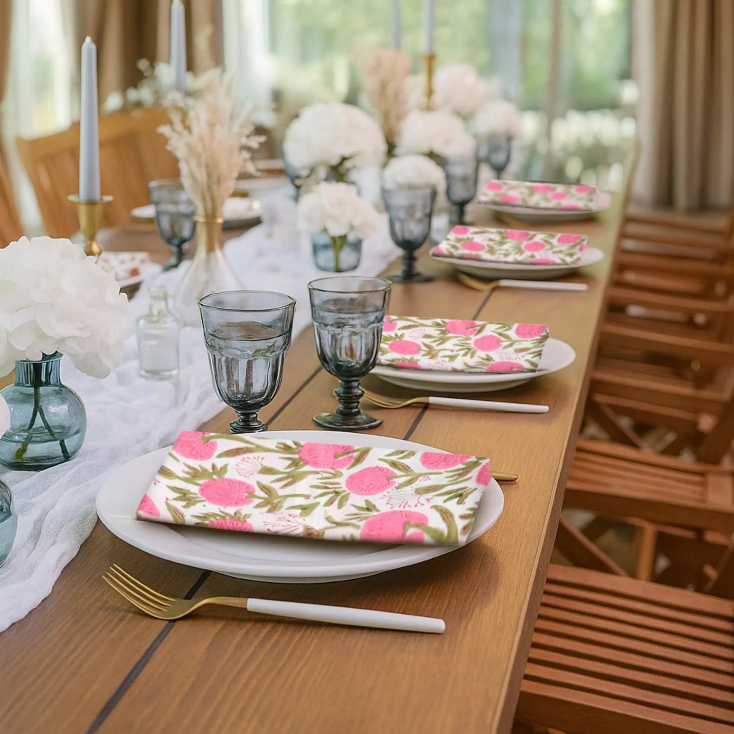 Dining table set with floral napkins, glasses, and cutlery in a bright room.
