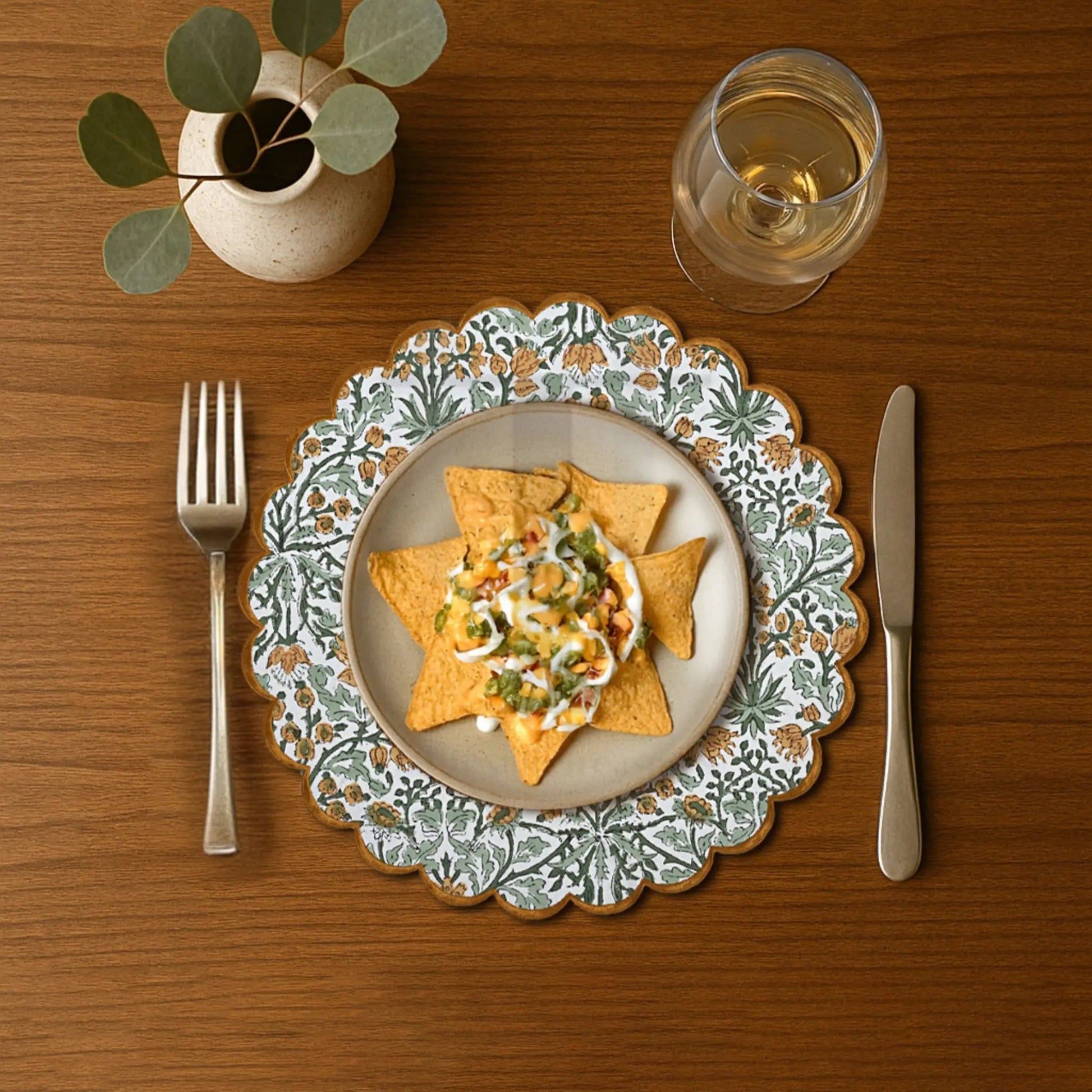 Dinner setting with a decorative plate of nachos, a glass of water, fork, and knife on a wooden table.